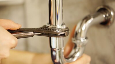 Plumber using wrench to perform maintenance on chrome drain pipe - Warren Brothers Plumbing serves Bastrop, Austin, and Elgin TX