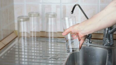Woman filling glass with clean filtered water from kitchen faucet - Warren Brothers Plumbing serves Bastrop, Austin, and Elgin TX